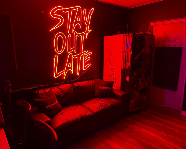 The image features a dimly lit room with a neon sign that reads "STAY OUT LATE," a dark sofa, and a door labeled "LABORATORY."