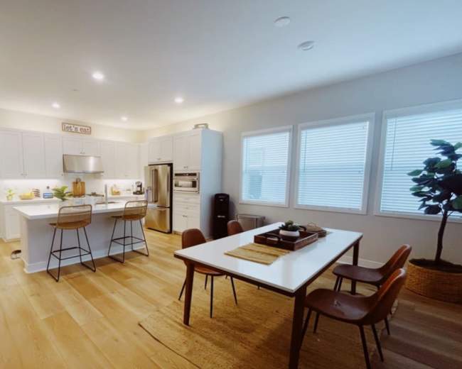 A modern kitchen features white cabinetry, a central island with bar stools, and a dining table surrounded by wooden chairs.