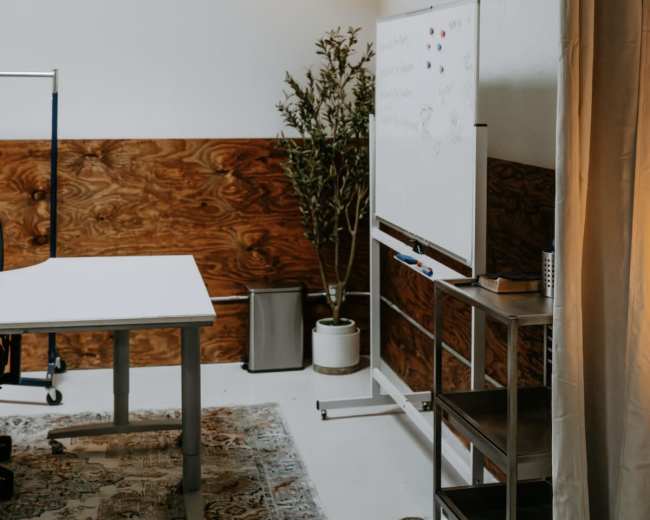 A modern office space features a whiteboard, a small plant, and a lamp, with wooden paneling on one wall and a light-colored table.