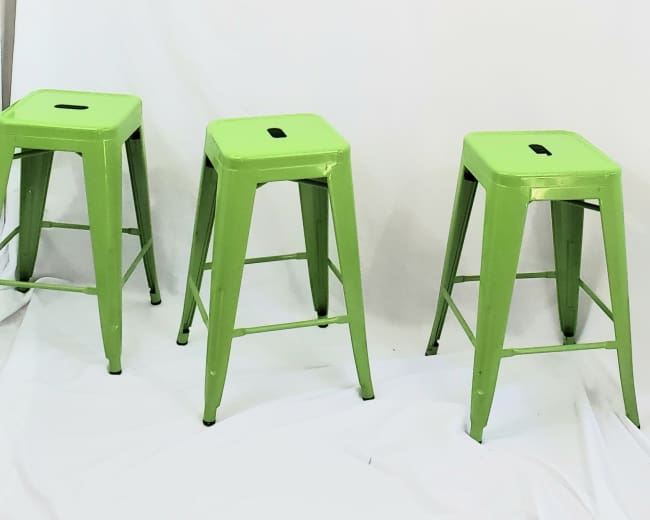 Three green metal stools are positioned in front of a white backdrop.