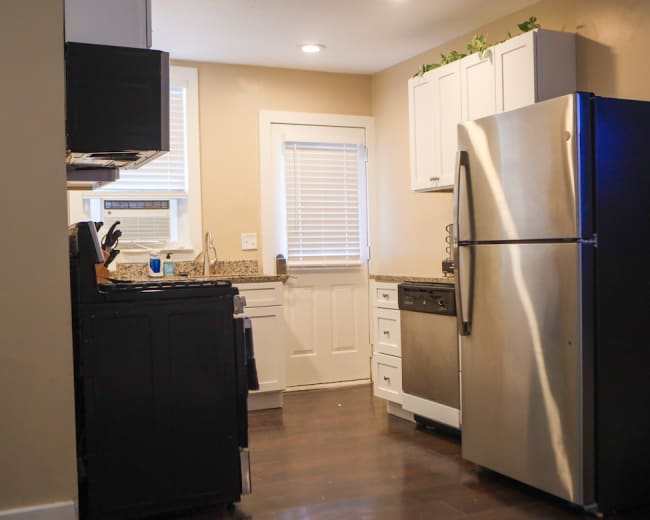 The image shows a compact kitchen featuring stainless steel appliances, dark cabinetry, and a window above the sink.