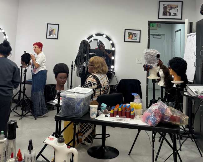 A cosmetology classroom features several students working on mannequins, with styling tools and various hair products displayed on a table.