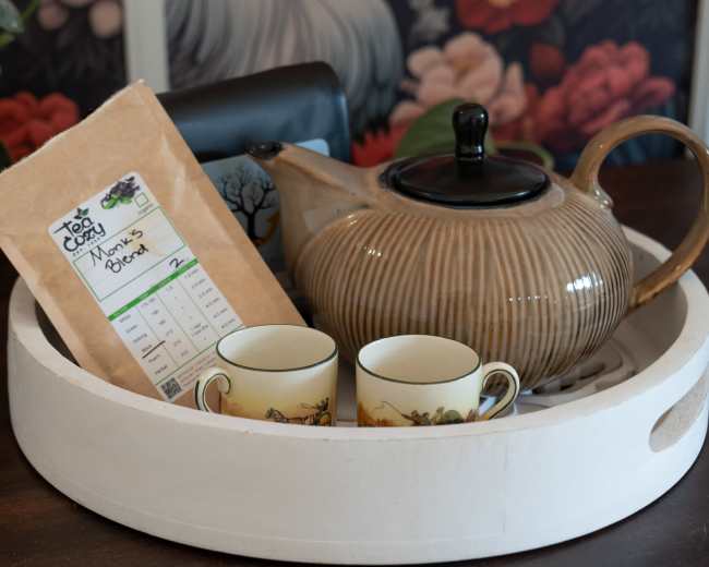 A teapot, a package of tea, and two decorative cups are arranged on a round tray.