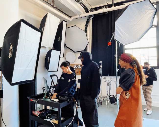 A group of individuals stands in a photography studio surrounded by various lighting equipment and backdrops.