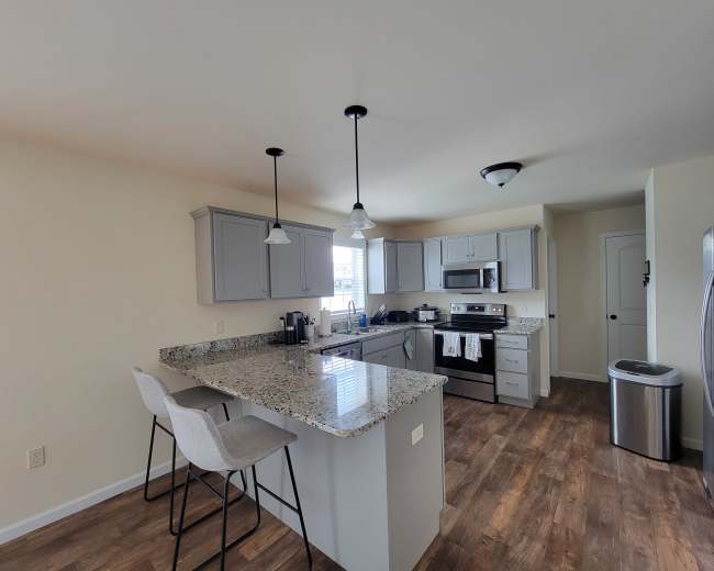 The image shows a modern kitchen with gray cabinets, a granite countertop, and stainless steel appliances.