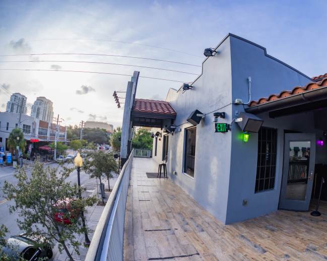 The image shows a building with a tiled roof and a balcony overlooking a street, featuring outdoor lights and adjacent urban scenery.