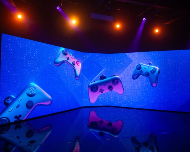 A large display screen showcases various gaming controllers against a blue background with vibrant lights.