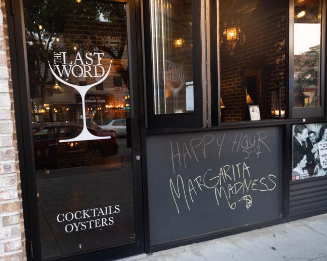 The exterior of a bar called "The Last Word" showcases a glass door with the establishment's name and an advertisement for a happy hour special promoting "Margarita Madness."