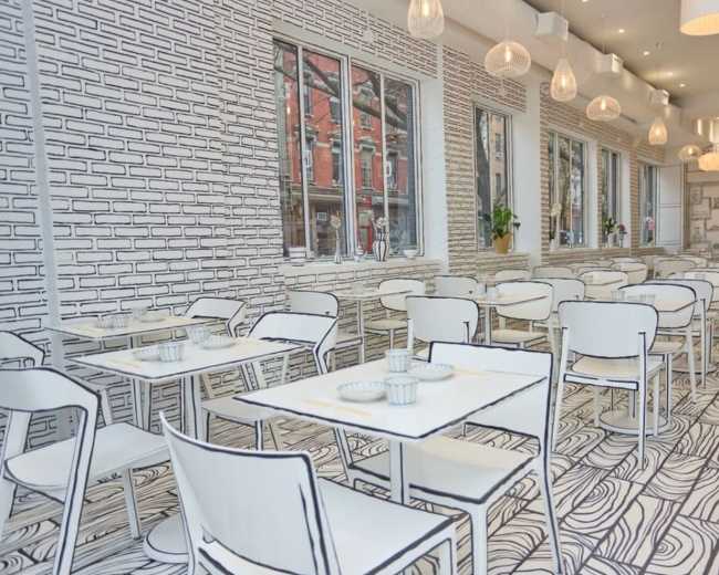 The image shows a restaurant with a minimalist design featuring tables and chairs, all in white, against a backdrop of hand-drawn brick and wood patterns on the walls and floor.