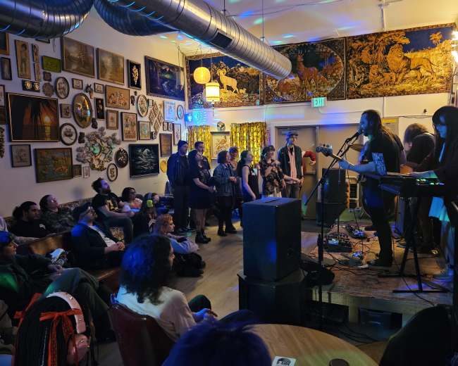 A band performs on stage in a decorated venue while an audience watches attentively.