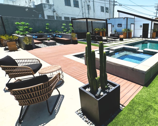 A contemporary backyard featuring a swimming pool, spa area, wooden decking, landscaped plants, and outdoor seating arrangements.