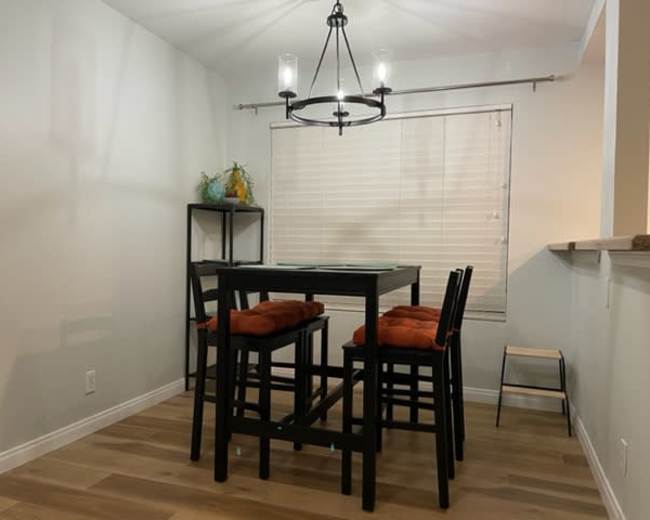 A dining area features a table with black chairs and orange cushions, illuminated by a chandelier above.