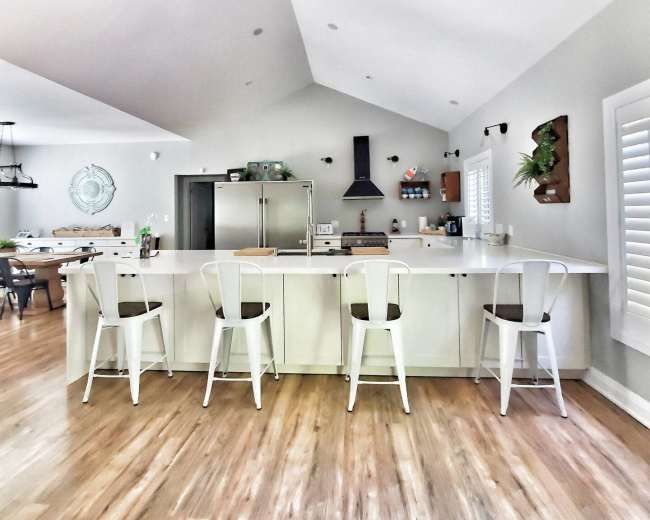The image shows a modern kitchen with a large island, four bar stools, and a vaulted ceiling.