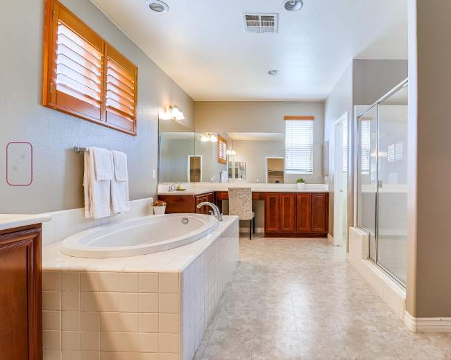 The image shows a spacious bathroom featuring a large soaking tub, a double vanity with wooden cabinets, and a separate glass shower.