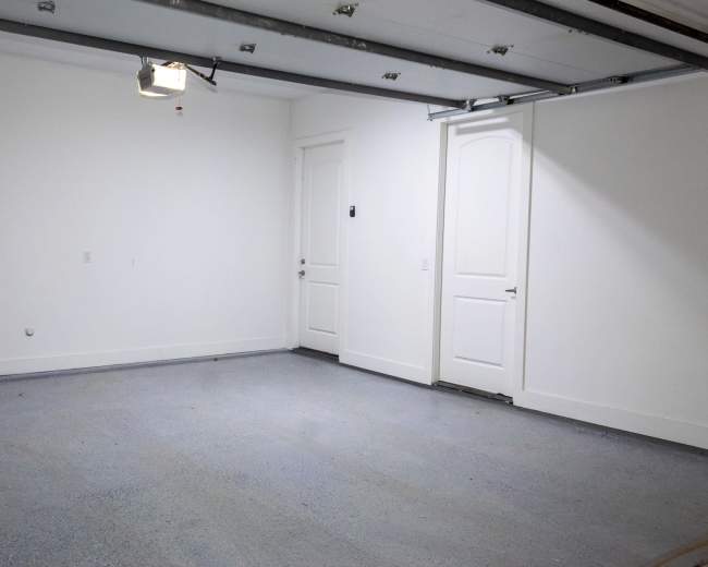 The image shows an empty garage with plain white walls, a concrete floor, and a closed garage door.