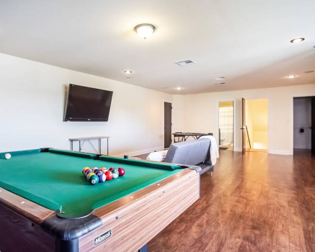 A room with a green pool table, a television mounted on the wall, and various furniture including a sofa and table.