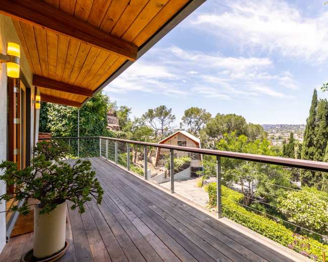 A spacious wooden deck with a railing overlooks a green landscape and distant hills under a blue sky.