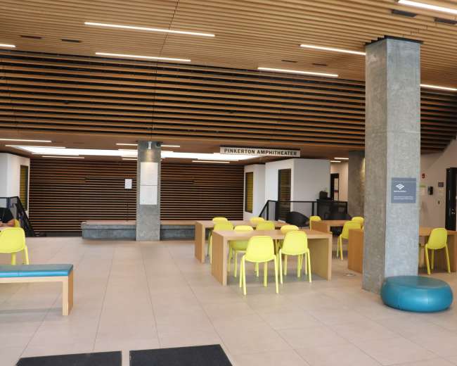 The image shows a spacious interior with seating areas, a large communal table, and a sign indicating the "Pinkerton Amphitheater."