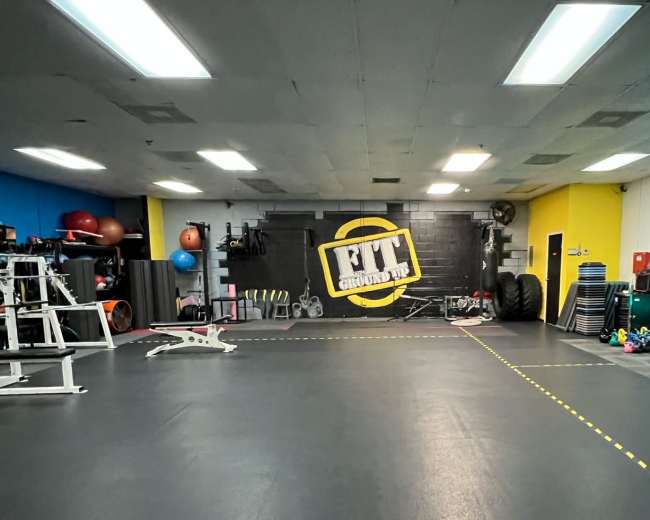 A well-equipped gym interior featuring various fitness equipment, exercise balls, and a large logo on the wall.