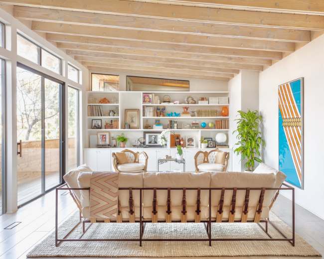 A spacious living room with a wooden ceiling, a large bookshelf filled with decorative items and books, and a seating arrangement centered around a coffee table.