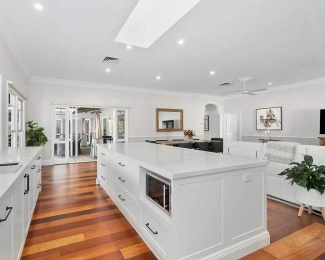 The image shows a modern, spacious kitchen with an island, featuring white cabinetry and wooden flooring.