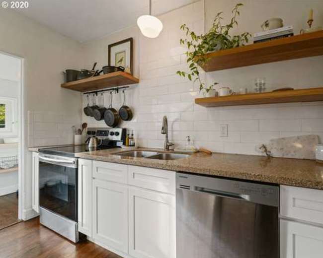 The image shows a modern kitchen with white cabinetry, granite countertops, and open shelves displaying cookware and plants.
