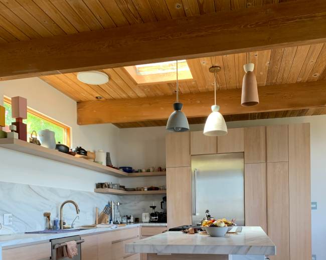 The kitchen features wooden beams, a central island with modern stools, and light-colored cabinetry with a marble accent.