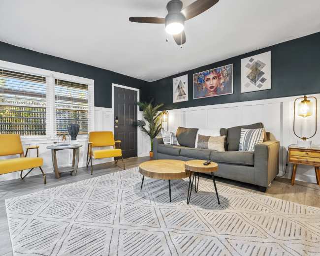 The living room features a gray sofa, two yellow armchairs, a coffee table, and framed artwork on the dark blue wall.