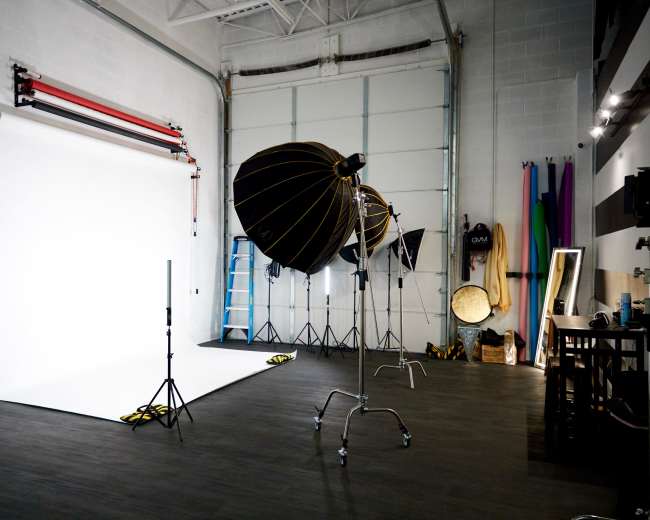A photography studio equipped with a white backdrop, lighting setups, and various props along the walls.