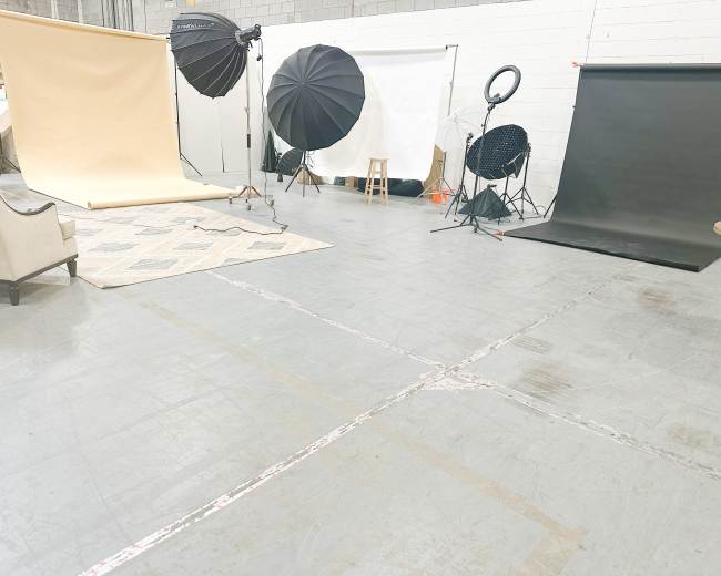 The image shows a photography studio setup with various backdrops, lighting equipment, and a chair on a patterned rug.