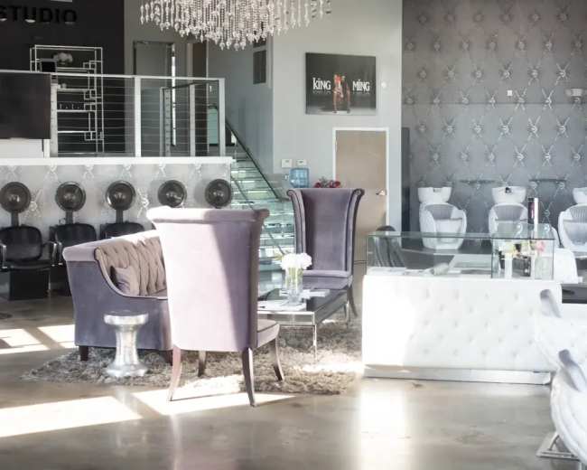 The image shows a modern, stylish salon interior featuring plush seating, a glass coffee table, and salon stations in the background.