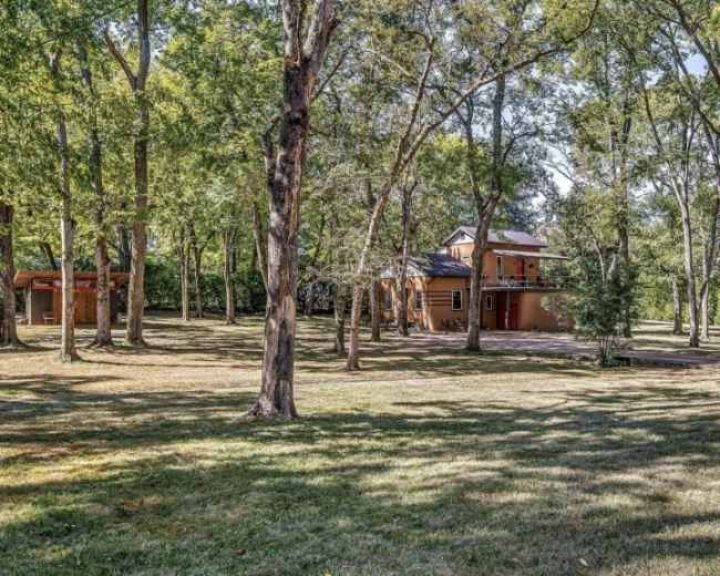 A two-story house is set among tall trees in a grassy area.