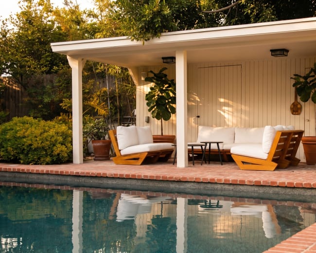 A modern poolside lounge area features white outdoor furniture and potted plants beside a swimming pool.