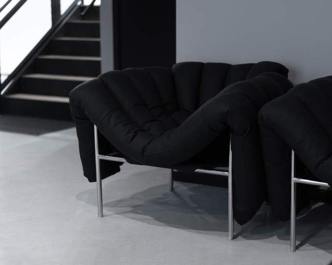 Two modern black upholstered chairs with silver metal frames are positioned next to each other in a minimalist interior space.
