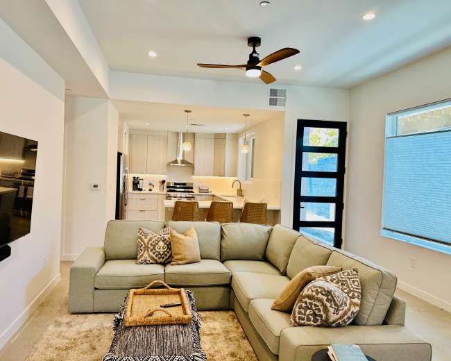 The image shows a modern living room with a large sectional sofa, a coffee table with decorative items, and an open kitchen visible in the background.