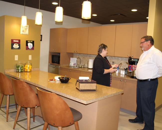 Two people are engaged in conversation in a modern kitchen area with a bar-style countertop and pendant lighting.