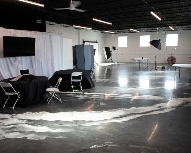 A spacious studio with polished gray floors, several tables and chairs, and various photography equipment set up.