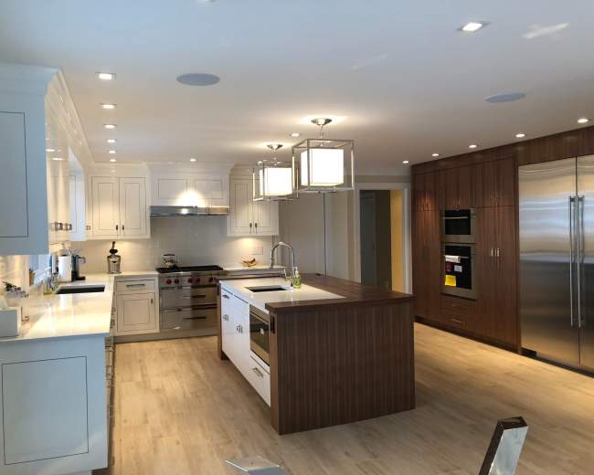The image shows a modern kitchen with white cabinets, a large island, stainless steel appliances, and two hanging light fixtures.