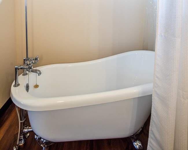 A vintage-style clawfoot bathtub with a showerhead and curtain, positioned near a window in a bathroom.