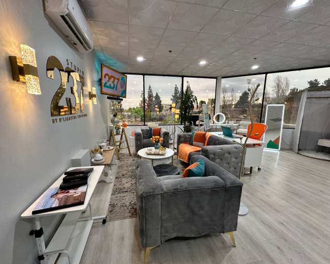 The image shows a modern, well-lit lounge area with comfortable furniture, a decorative rug, and large windows offering a view of the outdoors.