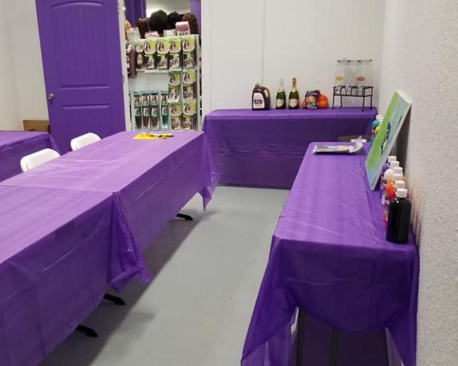 A room with several purple-covered tables and a small bar area, set up for an event or gathering.