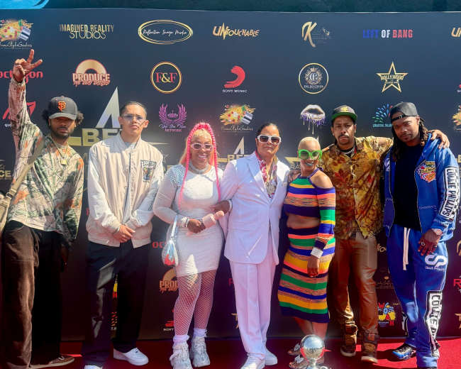 A group of six people poses on a red carpet in front of a backdrop featuring various logos and sponsors.