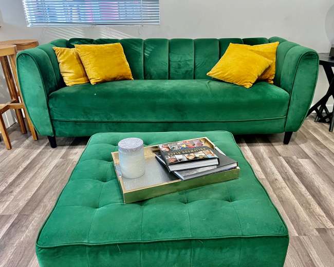 A green velvet couch with yellow cushions sits next to a square coffee table on a wood floor.