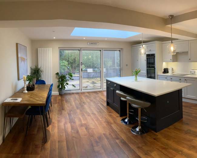 A modern kitchen features an island with seating, wooden flooring, and large sliding doors leading to an outdoor patio.