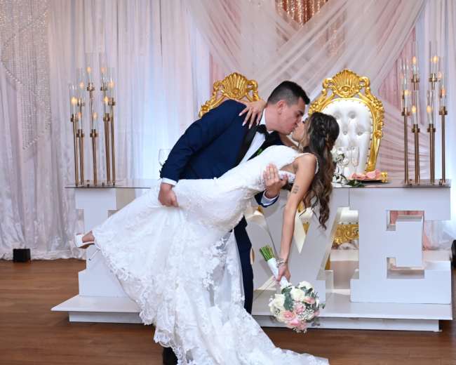 A couple shares a kiss as the groom lifts the bride in front of a decorative backdrop featuring the word "LOVE."