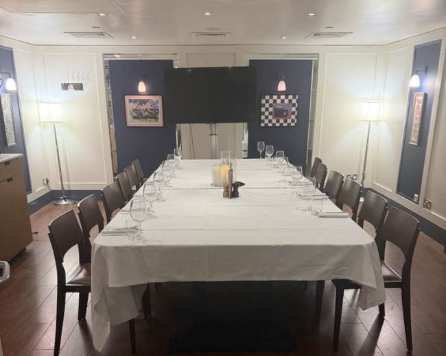 A long rectangular dining table is set with white tablecloth and glassware in a well-lit private dining room.