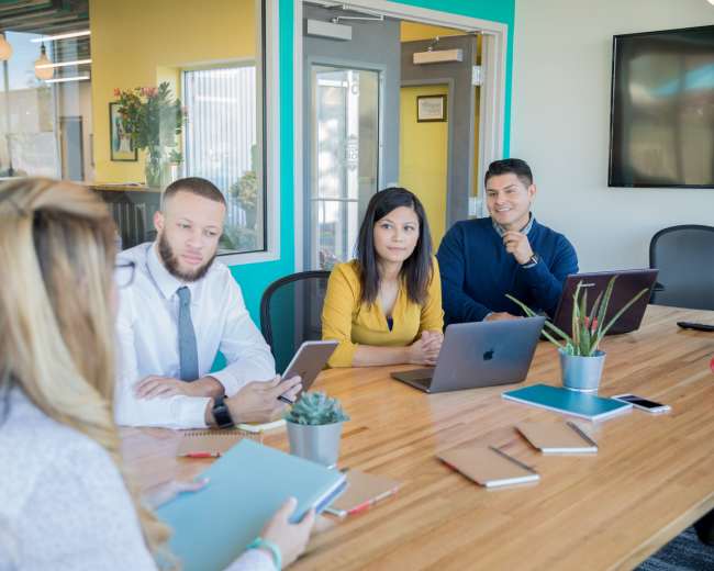 A group of four professionals engages in a meeting around a wooden table in a brightly colored office.