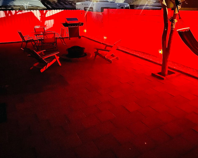 A patio area features a grill, seating, and a hammock, all illuminated by red lights against a contrasting wall.