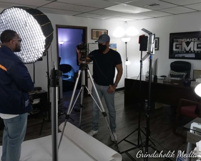 Two individuals are setting up a camera and lighting equipment in an office space for a photo or video shoot.