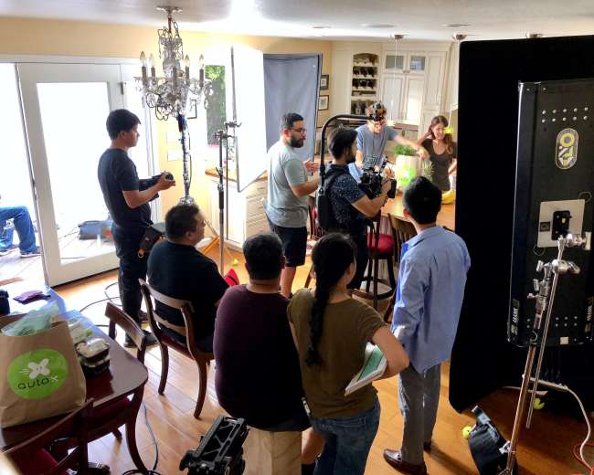A film crew is set up in a kitchen, preparing to film a scene with multiple cameras and lighting equipment.